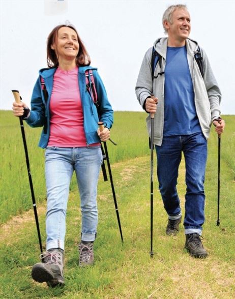 a middle aged man and woman who are nordic walking on an open path