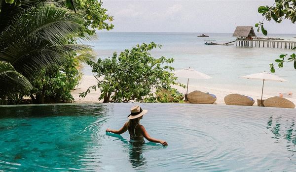 a woman in an infinityi pool in a tropical setting.  she is looking out to sea.